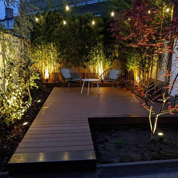 Éclairage extérieur d’une terrasse avec luminaires au sol et guirlande lumineuse