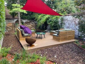 Coin détente de jardin avec terrasse en bois et voile d’ombrage rouge