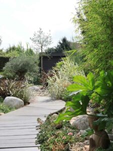 Allée sinueuse en bois composite entourée de plantes et graviers décoratifs