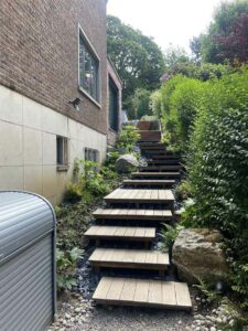 Escalier en bois sur graviers dans un jardin verdoyant en pente