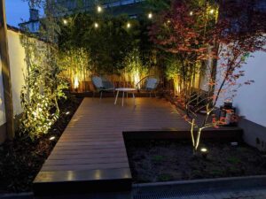 Terrasse bois de jardin éclairée la nuit avec fauteuils et bambous