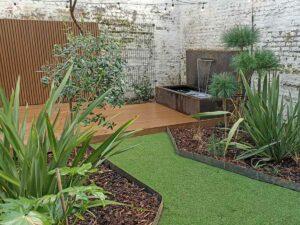 Fontaine murale en acier corten et terrasse bois dans un petit jardin urbain