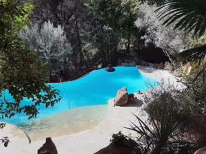 Piscine de forme libre entourée de roches et d’arbres méditerranéens