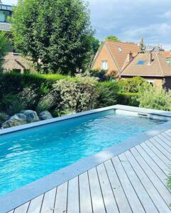 Piscine design rectangulaire avec terrasse en bois et végétation dense