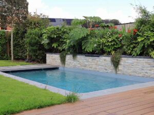 Piscine moderne bordée d’un mur de pierre et de plantes tropicales
