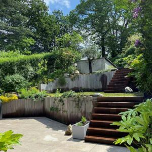 Aménagement de jardin en terrasses avec escaliers en bois, murs végétalisés et espace détente en pierre