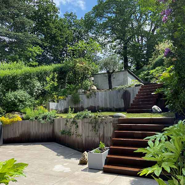 Aménagement de jardin en terrasses avec escaliers en bois, murs végétalisés et espace détente en pierre