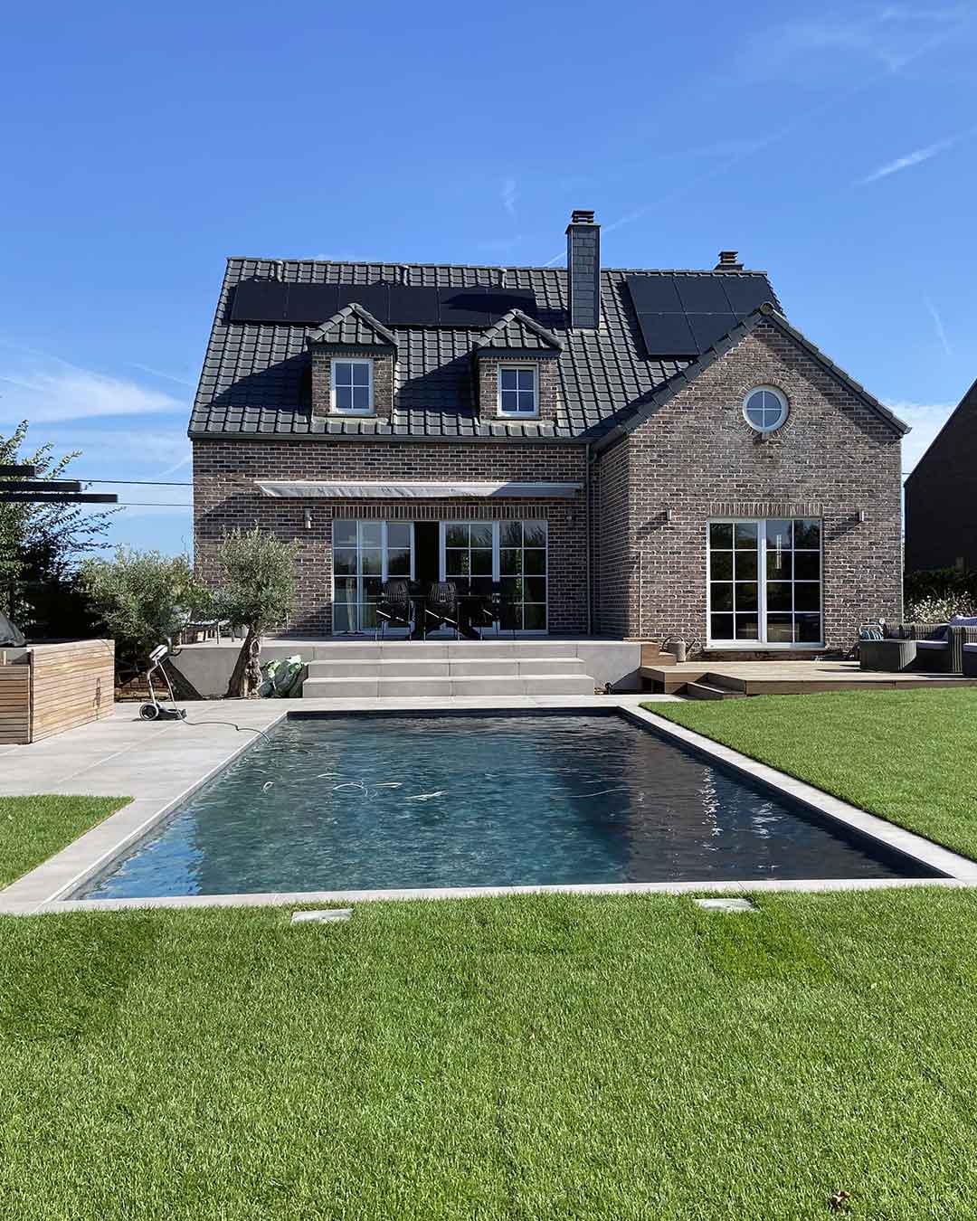Piscine contemporaine rectangulaire devant une maison en briques avec pelouse
