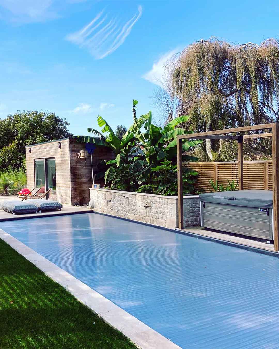 Piscine moderne avec volet roulant et jardin exotique attenant à un pool house
