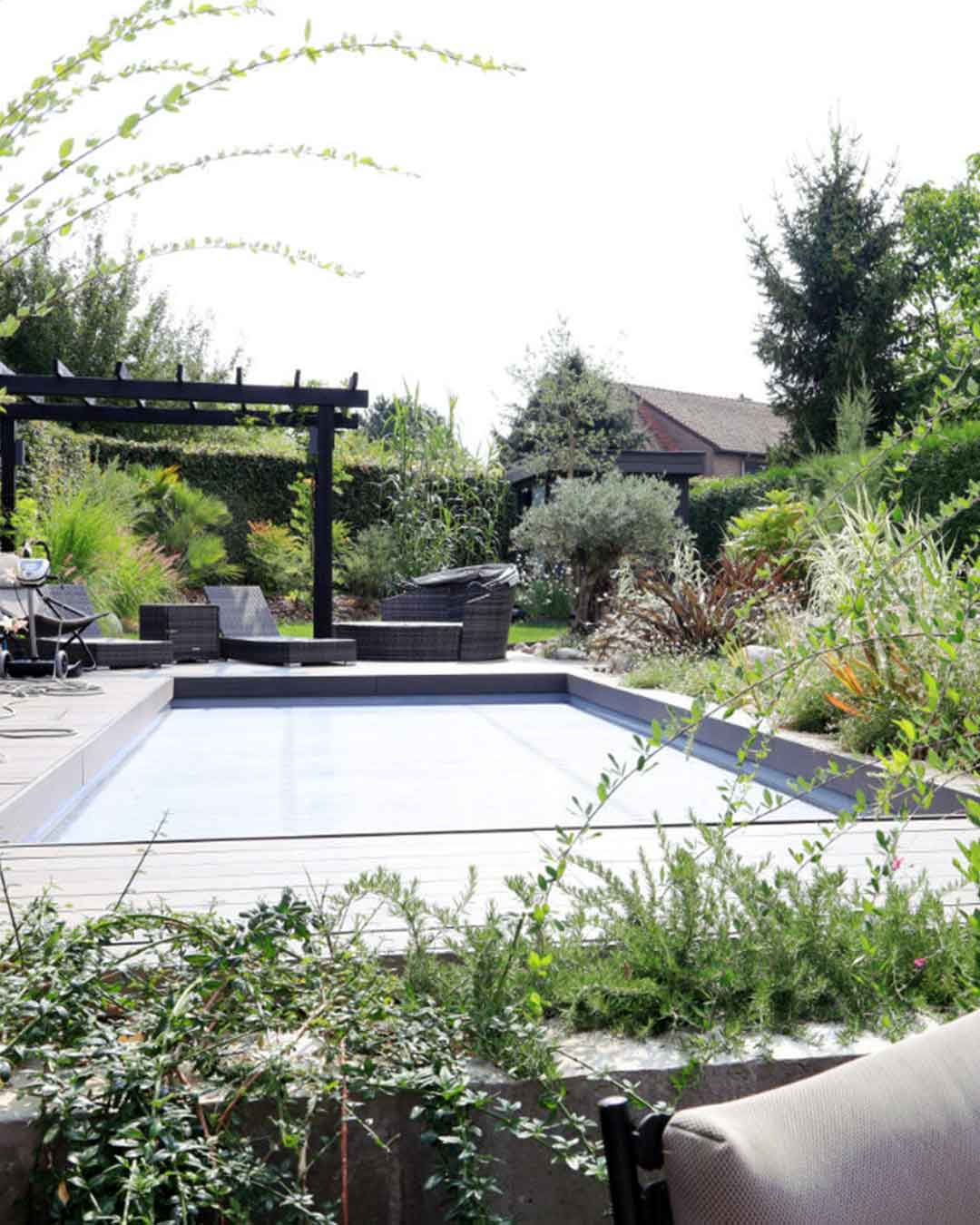 Piscine contemporaine entourée de végétation et d’un salon de jardin sous pergola