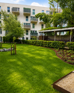Cour paysagère résidentielle avec pelouse, arbres et espaces verts au pied d’un immeuble moderne.
